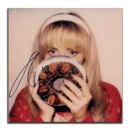 Woman in a red sweater holds a chocolate pecan cake next to an autographed Sabrina Carpenter FRUITCAKE green vinyl LP.
